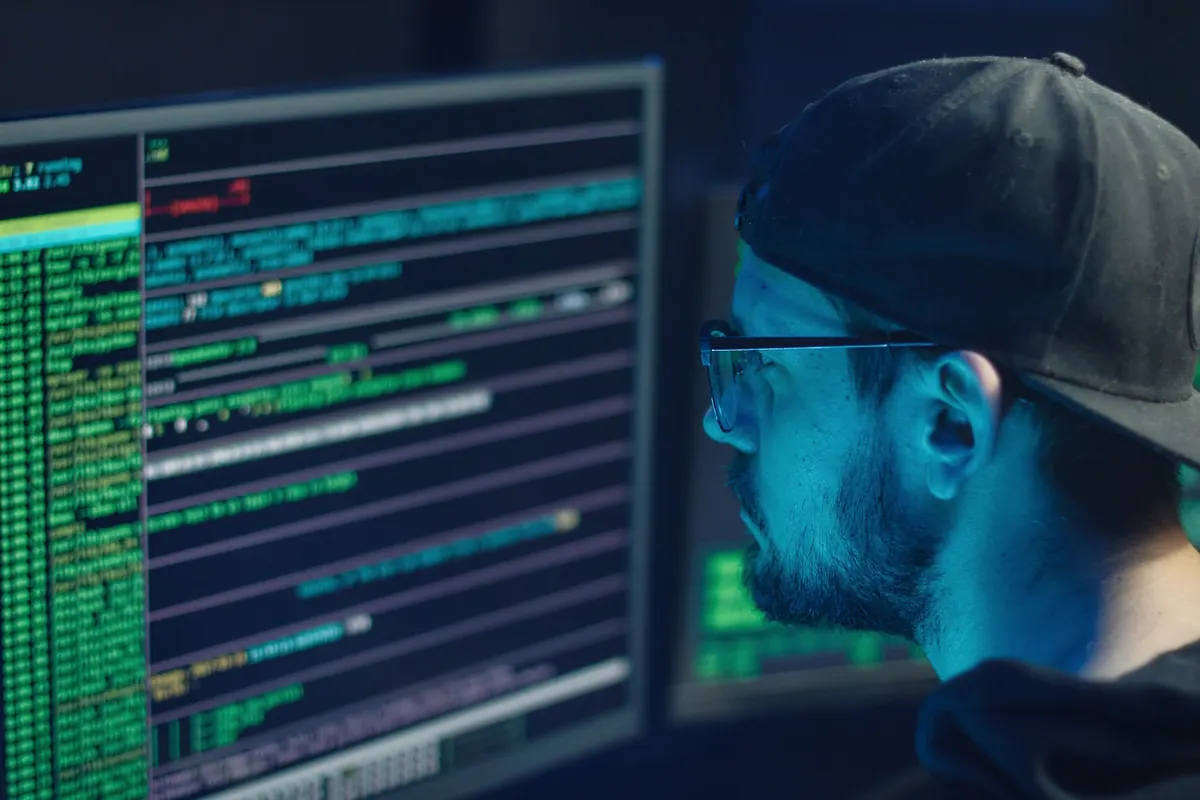 Analyst reviewing code on multiple monitors in a dim office