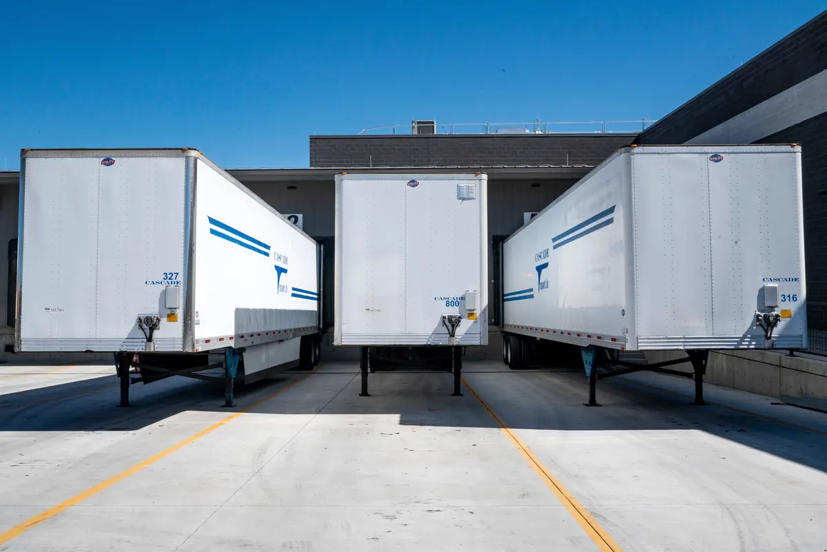 Three white freight trailers parked at loading docks under a blue sky