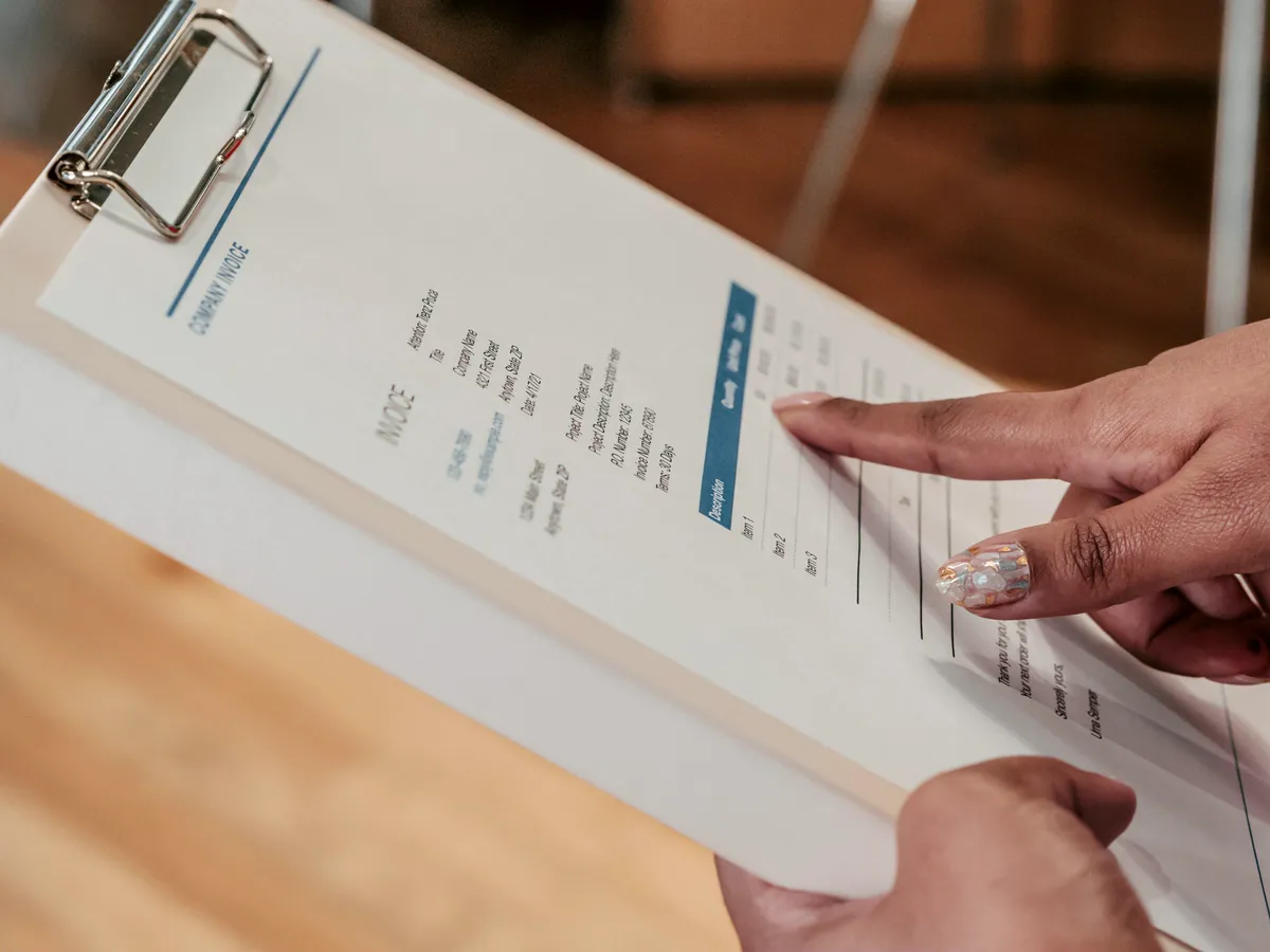 Person pointing at a line on an invoice held on a clipboard