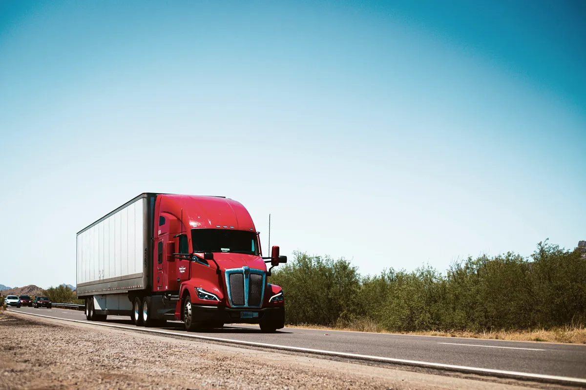 Red Kenworth T680 semi-truck pulling a dry van down an open highway