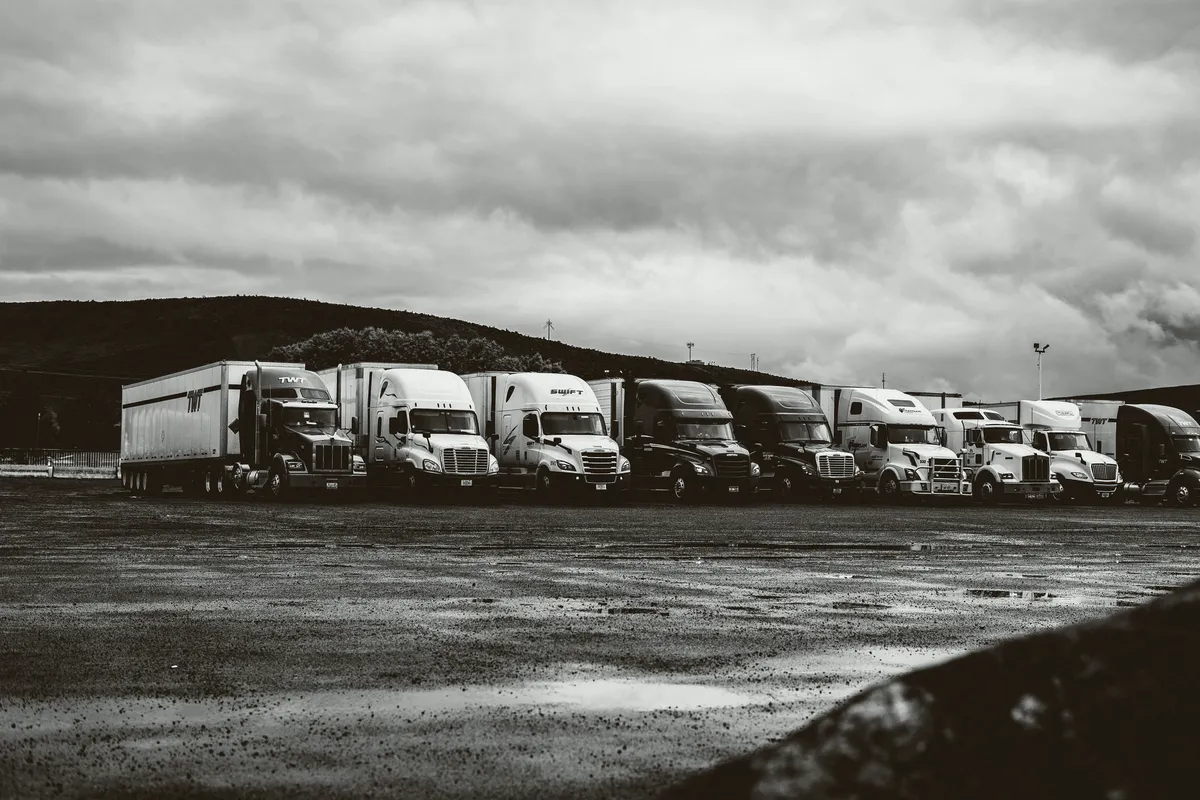 Row of parked semi-trucks in a rainy freight yard, in black and white